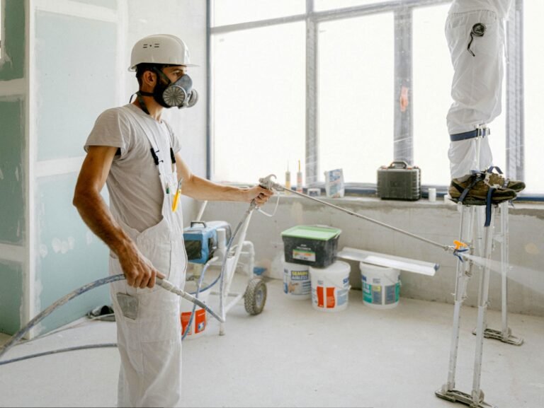 Pintor profesional aplicando pintura blanca con maquina en las paredes de un piso