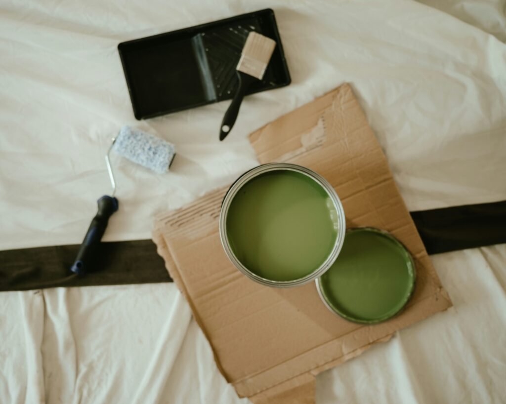 Rodillo, brocha y cubeta de pintura sobre suelo protegido con plástico, materiales de un pintor profesional durante reforma