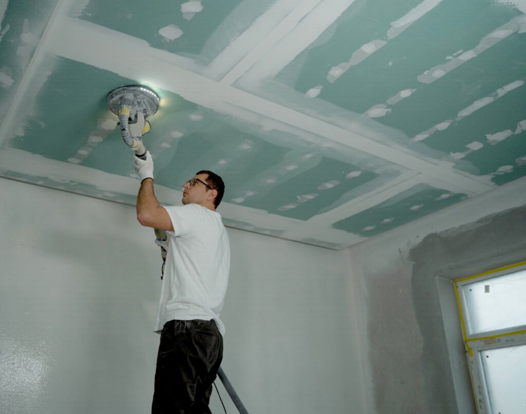 Trabajador lijando un cielo raso de pladur con maquina